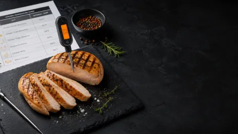 Grilované kuřecí prso s digitálním teploměrem na tmavém pozadí